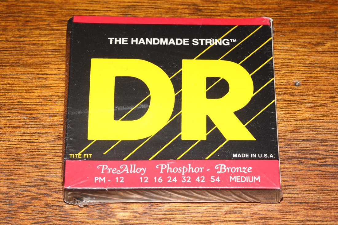 DR Pre-Alloy phosphor-bronze acoustic guitar strings photographed on a wooden surface.